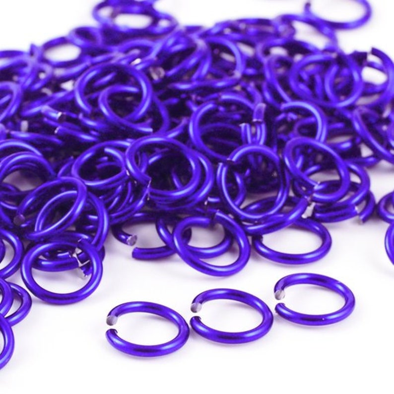 May include: A large pile of small, purple metal jump rings. The rings are all the same size and are arranged in a random pattern.