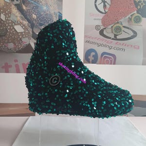 May include: A dark green sequined roller skate boot. The boot is covered in small, shiny, dark green sequins. The boot is displayed on a clear stand, with a logo in the background. The boot is a unique and eye-catching accessory.
