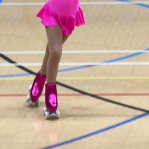 Puede incluir: Una persona joven que lleva un leotardo rosa y patines de ruedas rosas con ruedas blancas. La persona est&aacute; patinando en un suelo de madera con l&iacute;neas azules y amarillas.