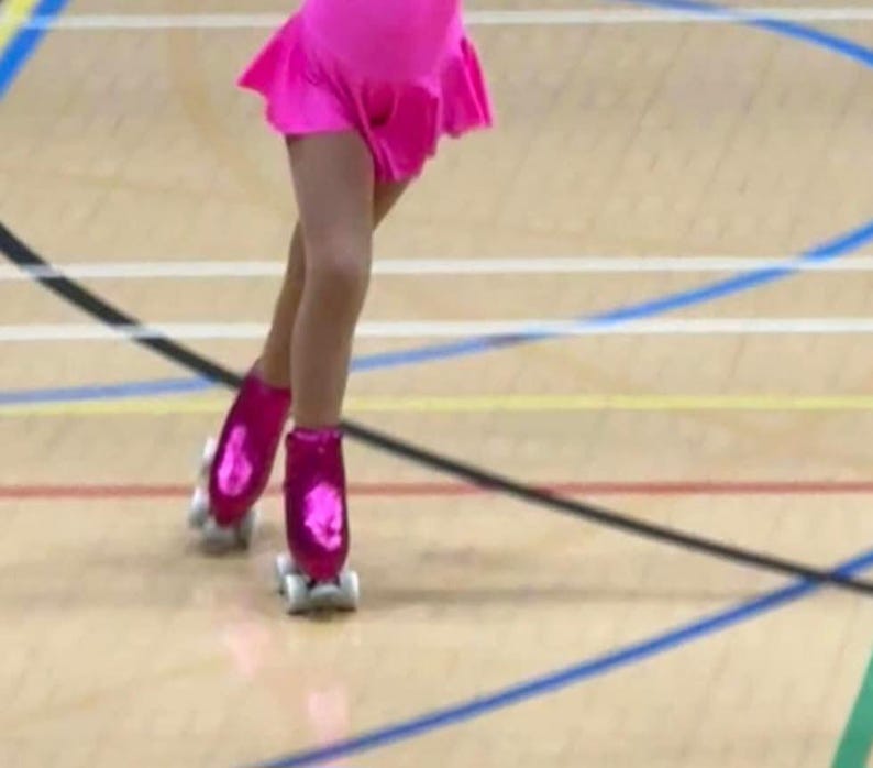 Puede incluir: Una persona joven que lleva un leotardo rosa y patines de ruedas rosas con ruedas blancas. La persona est&aacute; patinando en un suelo de madera con l&iacute;neas azules y amarillas.