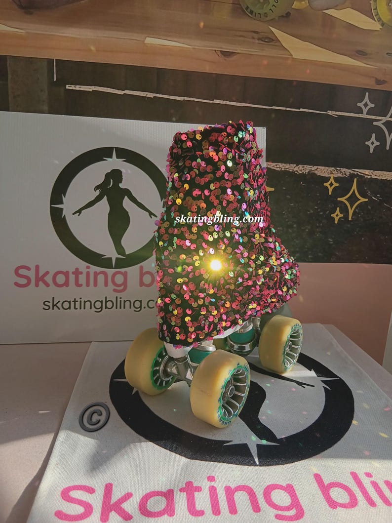 May include: A pair of roller skates with a black and pink sequined boot cover. The boot cover has a rainbow iridescent sheen. The skates are on a white surface with a black and white logo that says "skating bling.com".