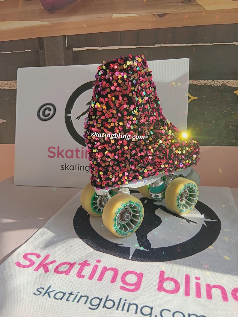 May include: Pink, black, and gold roller skate boot with sequins. The boot is on a white surface with a black circle and the text "skatingbling.com".