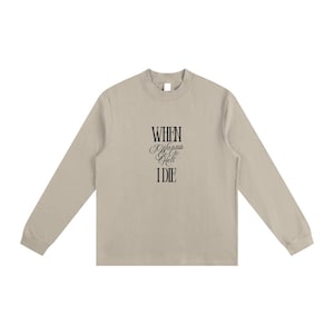 May include: A long-sleeved, beige shirt featuring the text "WHEN I Wanna Go To Hell I DIE" in black script. The shirt has a crew neck and a relaxed fit, suitable for casual wear.