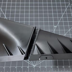 May include: Two black 3D printed parts with a geometric design. The parts are made of a smooth, matte black plastic. The parts are designed to be joined together.