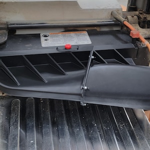 May include: Black dust collection system for a wood planer. The system has a large, curved, black plastic tube with a metal connector. The tube is attached to a black plastic housing with a series of vertical slats.
