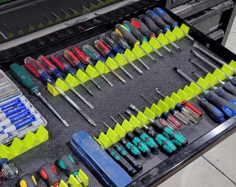 May include: A collection of various screwdrivers organized in a tool drawer using bright neon green plastic holders. The screwdrivers feature diverse handle colors including red, blue, black, green, and clear, with metal shafts and tips.