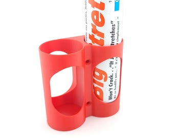 May include: A bright red plastic holder with two cylindrical compartments. One compartment holds a white and orange tube with the word "tretches" and "Big" printed on it. The holder has a curved design with a cutout.