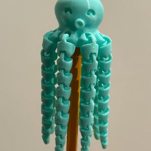 May include: A light blue 3D-printed octopus toy with articulated tentacles. The octopus is perched on a yellow pencil, showcasing its design and structure. The toy's details are visible, highlighting its unique, playful aesthetic.