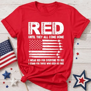 Könnte beinhalten: Ein rotes Kurzarm-T-Shirt mit weißem Text, der REMEMBER EVERYONE DEPLOYED UNTIL THEY ALL COME HOME, I WEAR RED FOR EVERYONE TO SEE, I STAND FOR THOSE WHO KEEP US FREE lautet, sowie einer Grafik einer amerikanischen Flagge mit Jet-Silhouetten.