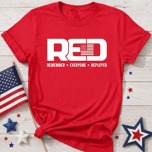 Könnte beinhalten: Ein leuchtend rotes Kurzarm-T-Shirt mit dem weißen Schriftzug RED, wobei die Buchstaben D ein amerikanisches Flaggendesign enthalten. Unter dem Haupttext stehen die weißen Wörter REMEMBER EVERYONE DEPLOYED, getrennt durch zwei kleine weiße Sterne.
