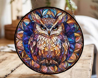 May include: A circular stained glass window depicting an owl. The owl has yellow eyes and is set against a backdrop of a colourful mosaic pattern in blue, purple, orange, and yellow. The window is framed in black and suspended by a chain.