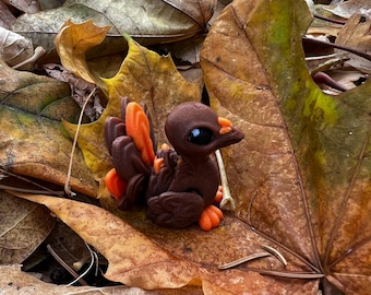 May include: A small, brown and orange bird figurine with large black eyes, sitting on a bed of autumn leaves.