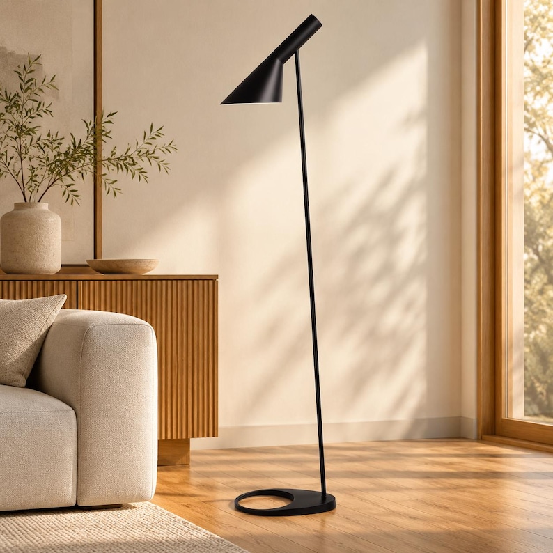 May include: A matte black floor lamp featuring a slender vertical pole, a circular base with an open center, and an adjustable conical shade that directs light downward. The lamp has a clean, streamlined silhouette with a simple metal construction.