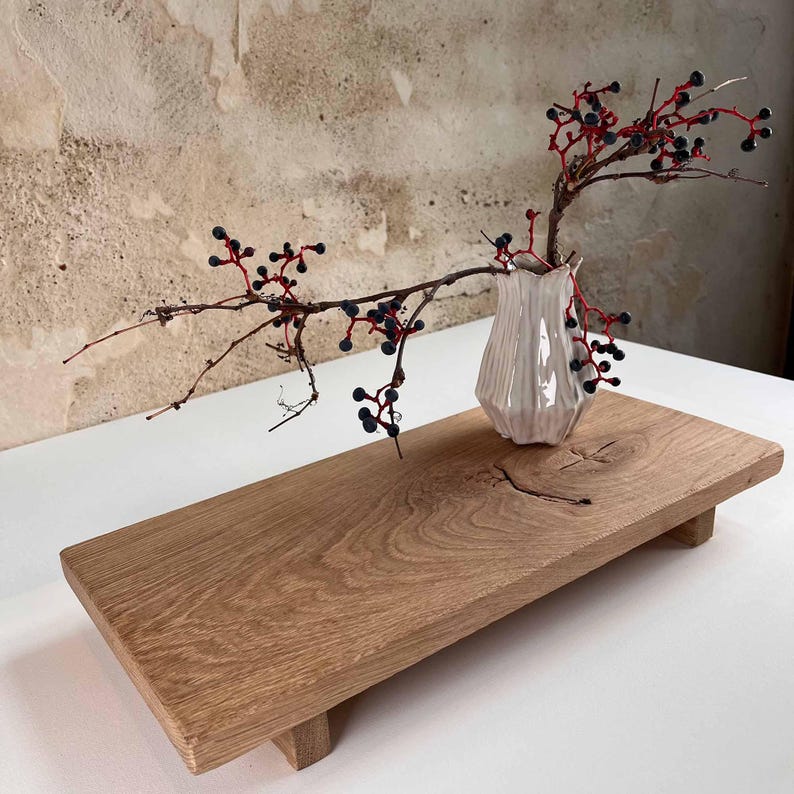 K&ouml;nnte beinhalten: Ein Holzserviertablett mit hellem Braunton, mit einer kleinen, wei&szlig;en, strukturierten Vase, die einen Zweig mit roten Stielen und dunklen Beeren h&auml;lt. Das Tablett ist rechteckig und ruht auf vier kurzen Beinen. Die Vase ist etwa 13 cm hoch.