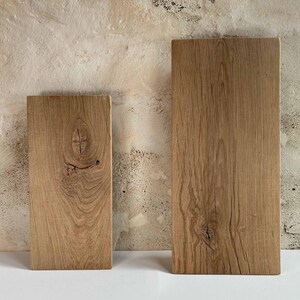 K&ouml;nnte beinhalten: Zwei rechteckige Holzbretter mit nat&uuml;rlicher Maserung. Die Bretter sind unterschiedlich gro&szlig;, das kleinere links. Das Holz hat eine warme, hellbraune Farbe und sichtbare Knoten.
