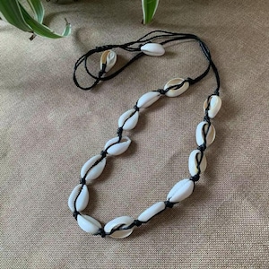 May include: A necklace made of white seashells strung on black cord. The shells are oval-shaped and evenly spaced along the cord. The necklace is a natural, beach-inspired accessory.