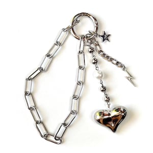 May include: A silver chain keychain with a heart charm, a pearl bead, and star and lightning bolt charms.