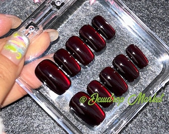 May include: A set of ten red, short, square-shaped fake nails in a clear plastic case. The nails have a glossy finish and are arranged in two rows. The case has a clear lid and a white label with the text "@Dewdrop Market".