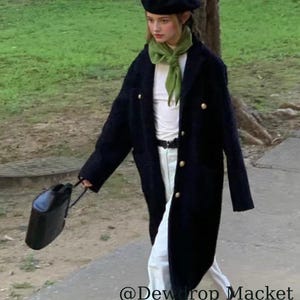 May include: A person wearing a black beret, a dark navy coat with gold buttons, a white top, white pants, and a green scarf. They are carrying a black handbag. The text "@Dewdrop Macket" is visible.