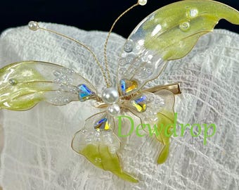 May include: A green and clear butterfly hair clip with a pearl and crystal accents. The clip is made of resin and has a delicate, feminine design.