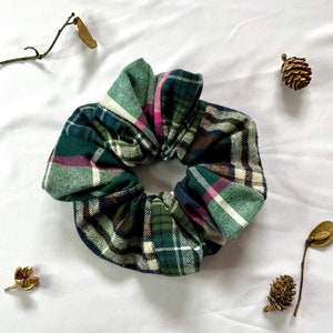 May include: Green, pink and white plaid scrunchie hair tie. The scrunchie is made of soft fabric and is perfect for adding a touch of style to any outfit.