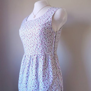 Peut inclure: Une robe blanche sans manches avec un petit imprim&eacute; floral dans les tons de violet, vert et bleu. La robe a un corsage ajust&eacute; et une jupe ample.