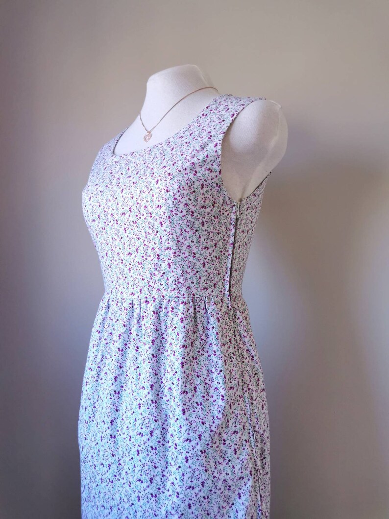 Peut inclure: Une robe blanche sans manches avec un petit imprim&eacute; floral dans les tons de violet, vert et bleu. La robe a un corsage ajust&eacute; et une jupe ample.