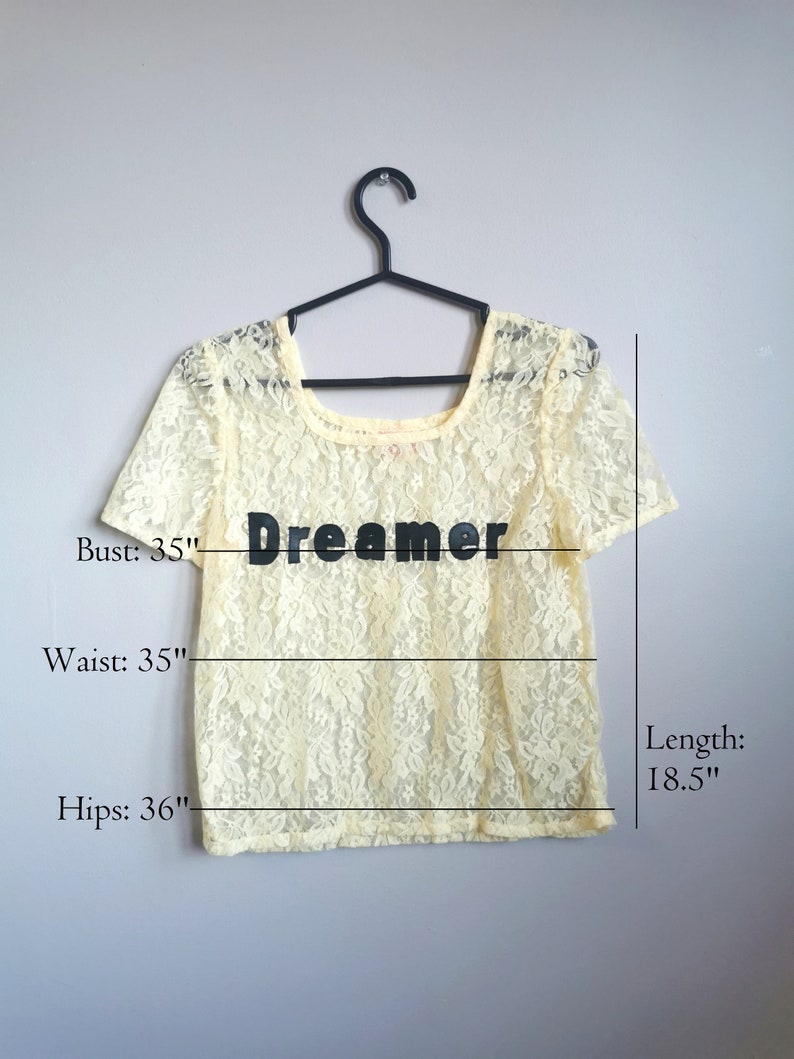 May include: A pale yellow lace top with a scoop neck and short sleeves. The top has the word "Dreamer" printed on the front. The top measures 35 inches in bust, 35 inches in waist, 36 inches in hips, and 18.5 inches in length.