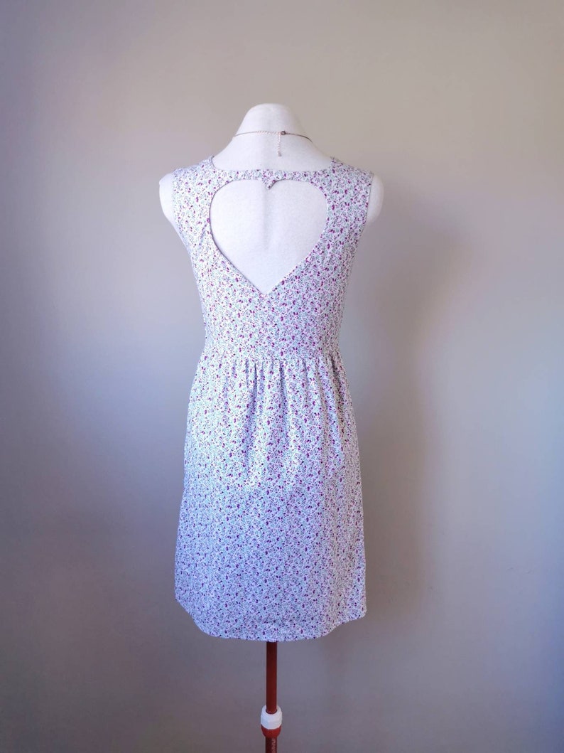 Peut inclure: Une robe blanche sans manches avec un imprim&eacute; floral et une d&eacute;coupe en forme de c&oelig;ur dans le dos.