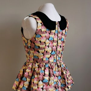 K&ouml;nnte beinhalten: Ein &auml;rmelloses Oberteil mit Cupcake-Druck in Schwarz und Wei&szlig;, einem schwarzen Peter-Pan-Kragen und einem R&uuml;schen-Saum.