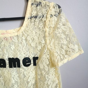 May include: A yellow lace top with short sleeves and the word "Dreamer" printed in black on the front.