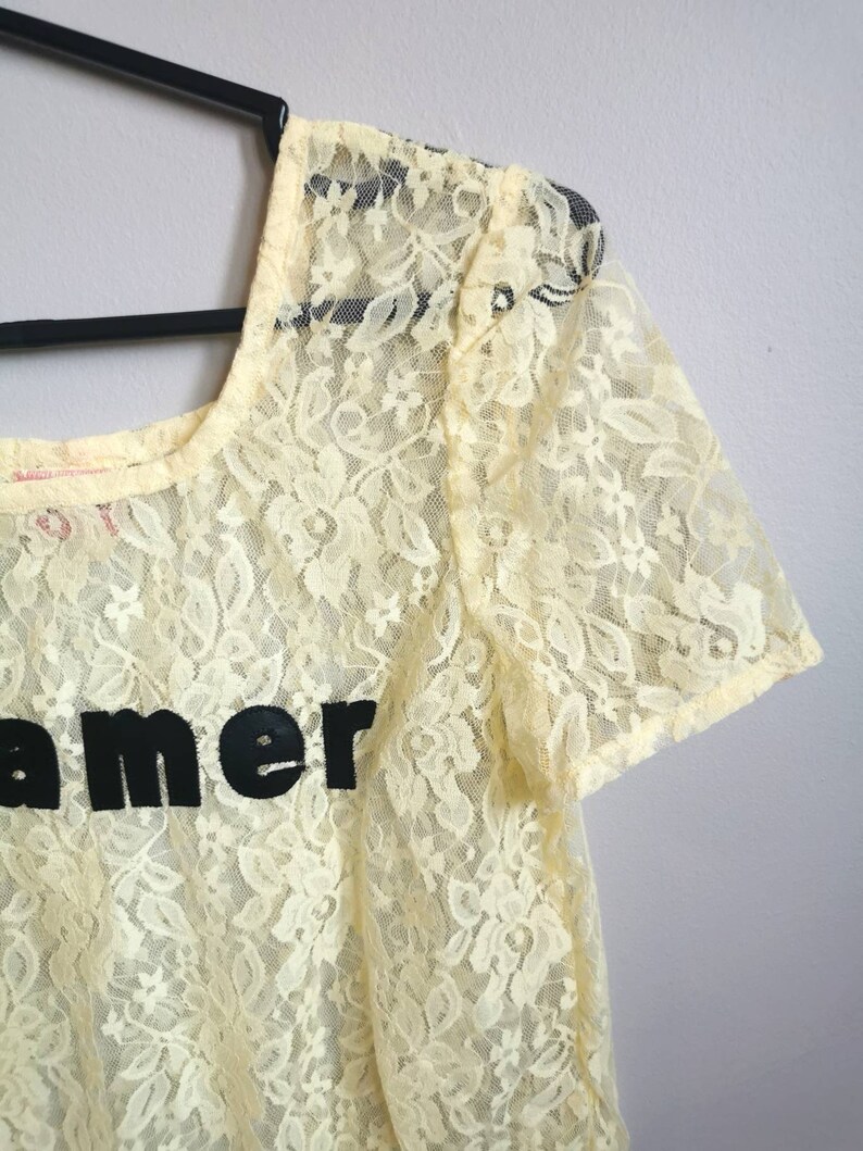 May include: A yellow lace top with short sleeves and the word "Dreamer" printed in black on the front.