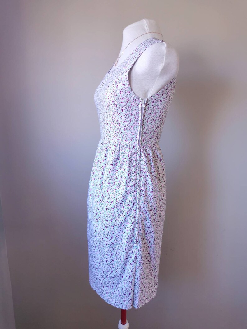 Peut inclure: Une robe blanche sans manches avec un petit imprim&eacute; floral dans les tons rose et bleu. La robe a un corsage ajust&eacute; et une jupe l&eacute;g&egrave;rement &eacute;vas&eacute;e.