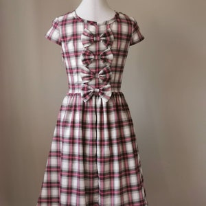 Puede incluir: Un vestido de cuadros blancos, rosas y negros con manga corta y un detalle de lazo en la parte delantera.