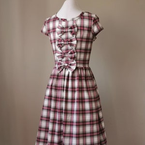 Puede incluir: Un vestido de cuadros blancos y rosas con un corpi&ntilde;o ajustado y una falda completa. El vestido tiene tres grandes lazos en la espalda, hechos del mismo tejido.