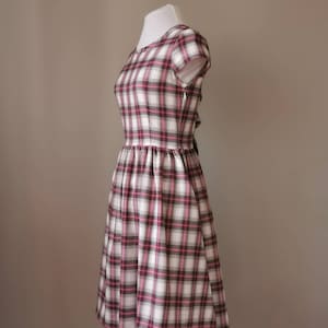 Puede incluir: Un vestido de cuadros blancos, rosas y negros con un corpi&ntilde;o ajustado y una falda completa. El vestido tiene mangas cortas y un escote redondo.
