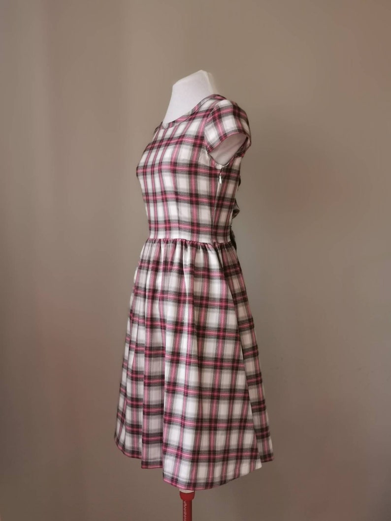 Puede incluir: Un vestido de cuadros blancos, rosas y negros con un corpi&ntilde;o ajustado y una falda completa. El vestido tiene mangas cortas y un escote redondo.