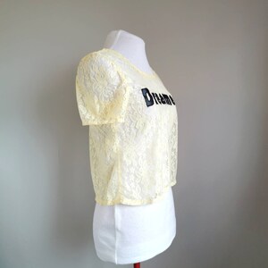 May include: A yellow lace crop top with short sleeves and the word "Dream" embroidered on the front.