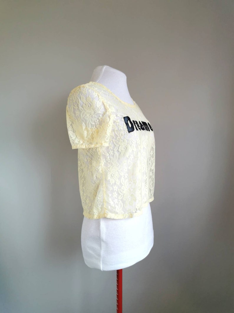 May include: A yellow lace crop top with short sleeves and the word "Dream" embroidered on the front.