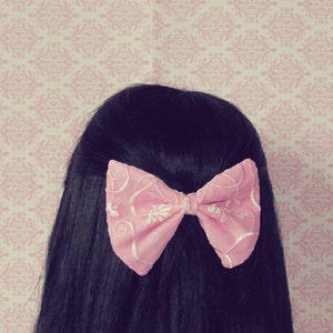 May include: A pink bow with a floral pattern is tied in a woman's black hair.