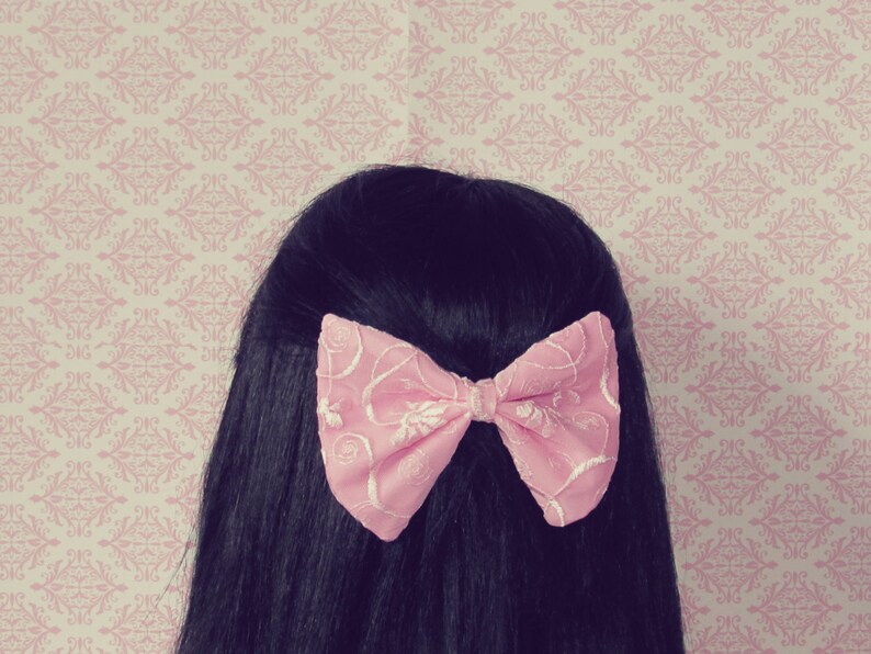 May include: A pink bow with a floral pattern is tied in a woman's black hair.