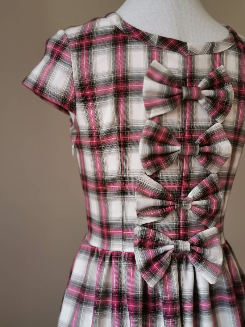 Puede incluir: Un vestido de cuadros blancos y rosas con tres grandes lazos en la espalda. Los lazos est&aacute;n hechos del mismo tejido de cuadros que el vestido.