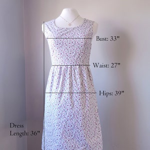 Peut inclure: Une robe blanche &agrave; petit imprim&eacute; floral dans les tons violet et rose. La robe a un col rond, des manches courtes et un corsage ajust&eacute; qui s'&eacute;vase en une jupe. La robe mesure 91 cm de long, 84 cm de tour de poitrine, 69 cm de tour de taille et 99 cm de tour de hanches. Le tissu a une &eacute;lasticit&eacute; minimale.