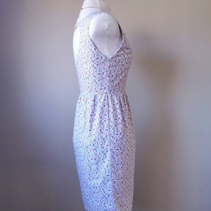 Peut inclure: Une robe blanche sans manches avec un petit imprim&eacute; floral dans les tons rose et violet. La robe a un corsage ajust&eacute; et une jupe l&eacute;g&egrave;rement &eacute;vas&eacute;e.