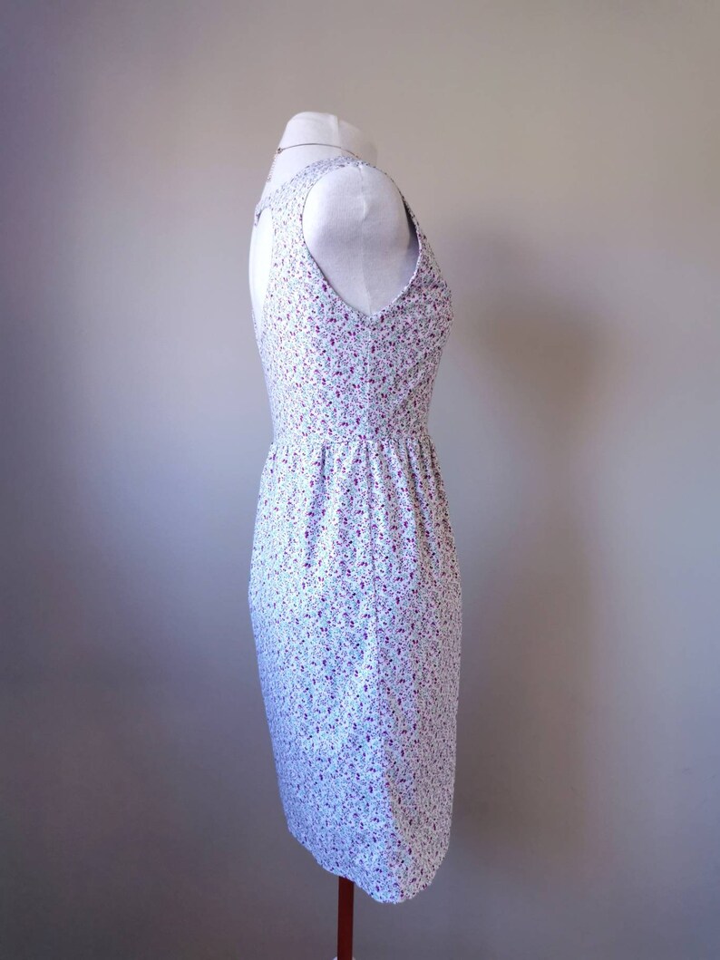 Peut inclure: Une robe blanche sans manches avec un petit imprim&eacute; floral dans les tons rose et violet. La robe a un corsage ajust&eacute; et une jupe l&eacute;g&egrave;rement &eacute;vas&eacute;e.