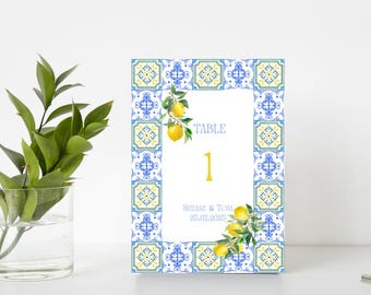Puede incluir: Una tarjeta de número de mesa blanca con un borde de patrón de azulejos azules y amarillos. La tarjeta tiene el texto "TABLE 1" y "Suzanne & Tom 25.01.2025".