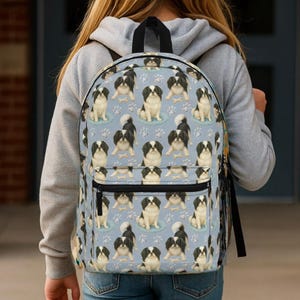 Könnte beinhalten: Ein hellblauer Rucksack mit einem sich wiederholenden Muster aus schwarz-weißen Hunden. Der Rucksack hat einen schwarzen Griff, eine Vordertasche und eine Seitentasche aus Mesh. Das Hundemuster enthält Pfotenabdrücke auf hellblauem Hintergrund.