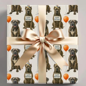 Puede incluir: Papel de regalo con un patrón repetido de perros marrones con gorros de fiesta y letreros que dicen "Feliz Cumpleaños". El diseño también incluye globos naranjas. El papel de regalo está atado con una cinta y un lazo dorados claros.