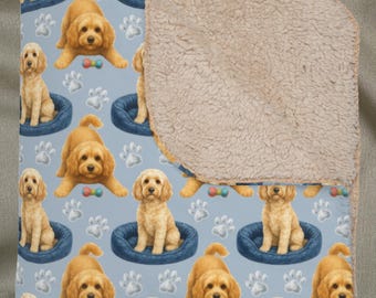 以下が含まれることがあります： 金色の犬、青い犬用ベッド、白い足跡の繰り返し模様が特徴の、明るい青色のブランケット。ブランケットは、柔らかいタン色のシェルパフリース裏地付き。犬は様々なポーズで描かれています。