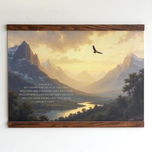 Op de afbeelding: Een ingelijste landschapsafdruk met een bergketen, een rivier en een vliegende adelaar tegen een zonsondergang. De afdruk bevat de tekst van Jesaja 40:31. Het frame is gemaakt van donker hout.